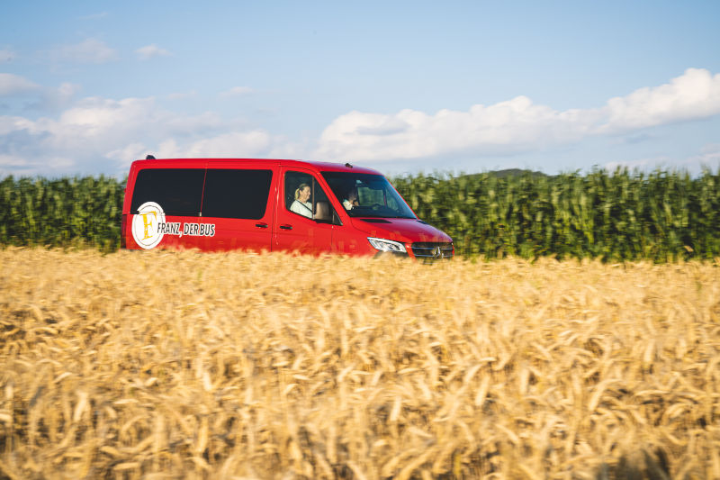 Franz, der Bus on Tour, im Vordergrund ist ein Weizenfeld zu sehen